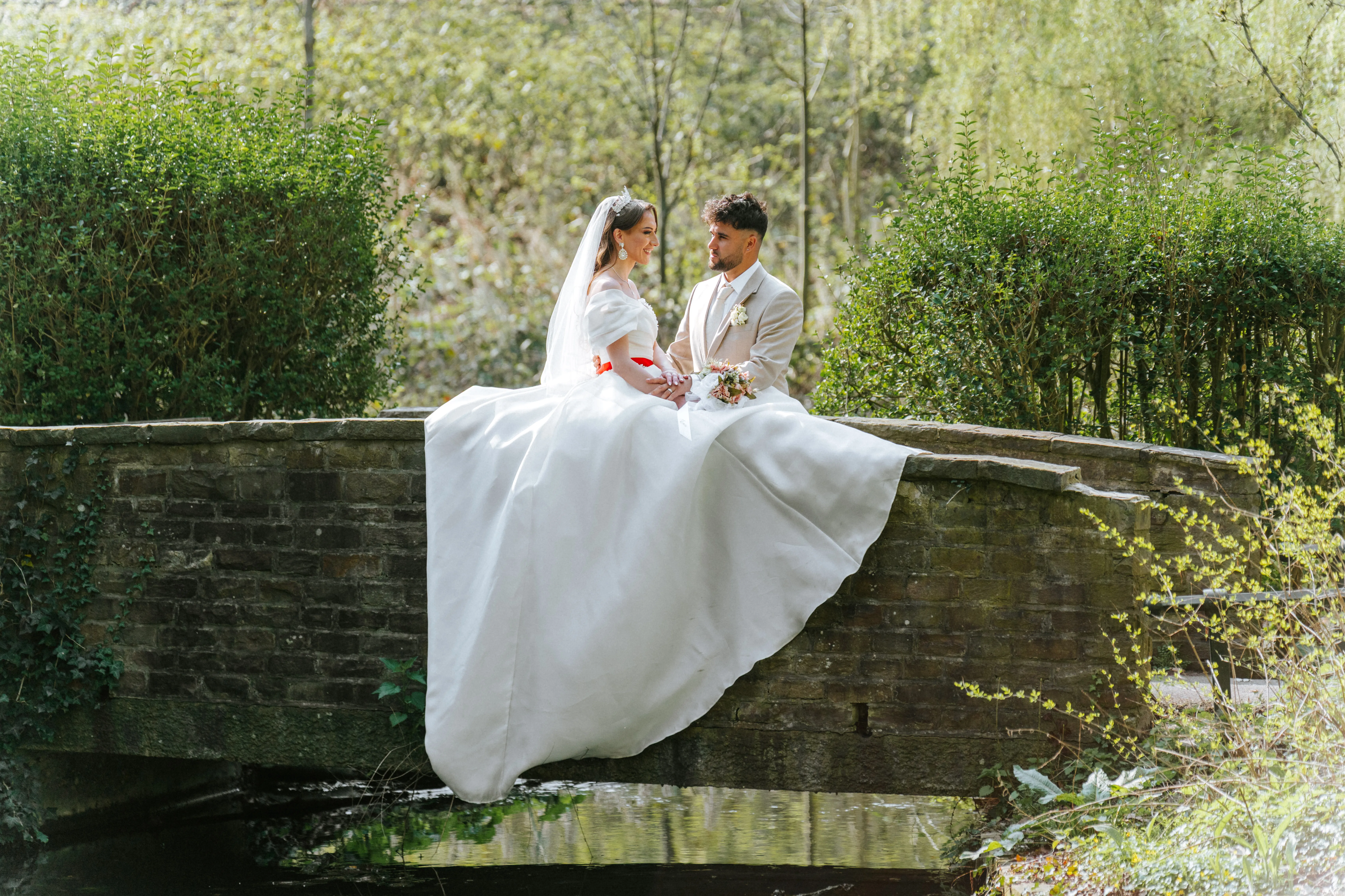 Shqipe et Emre assis sur un petit pont en pierre au milieu d'un jardin boisé