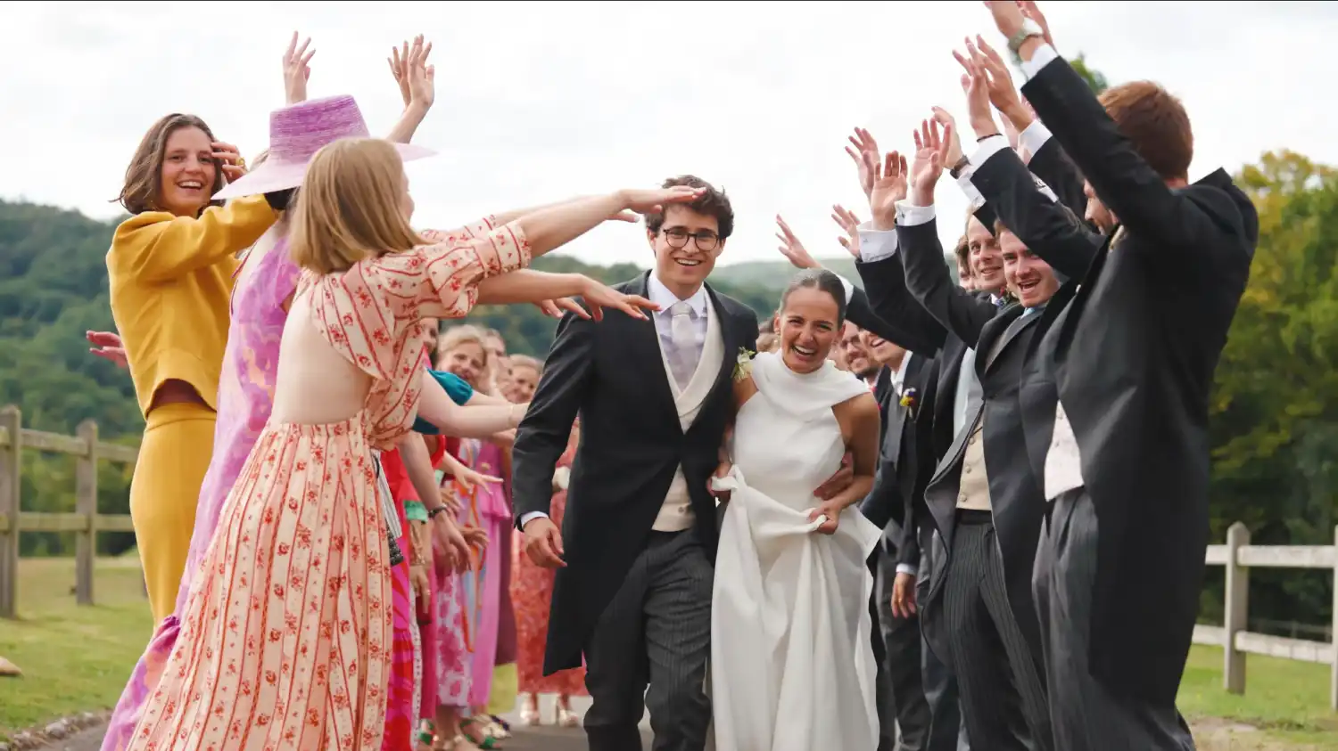 Stéphanie et Harold passant sous une haie d'honneur devant un paysage boisé